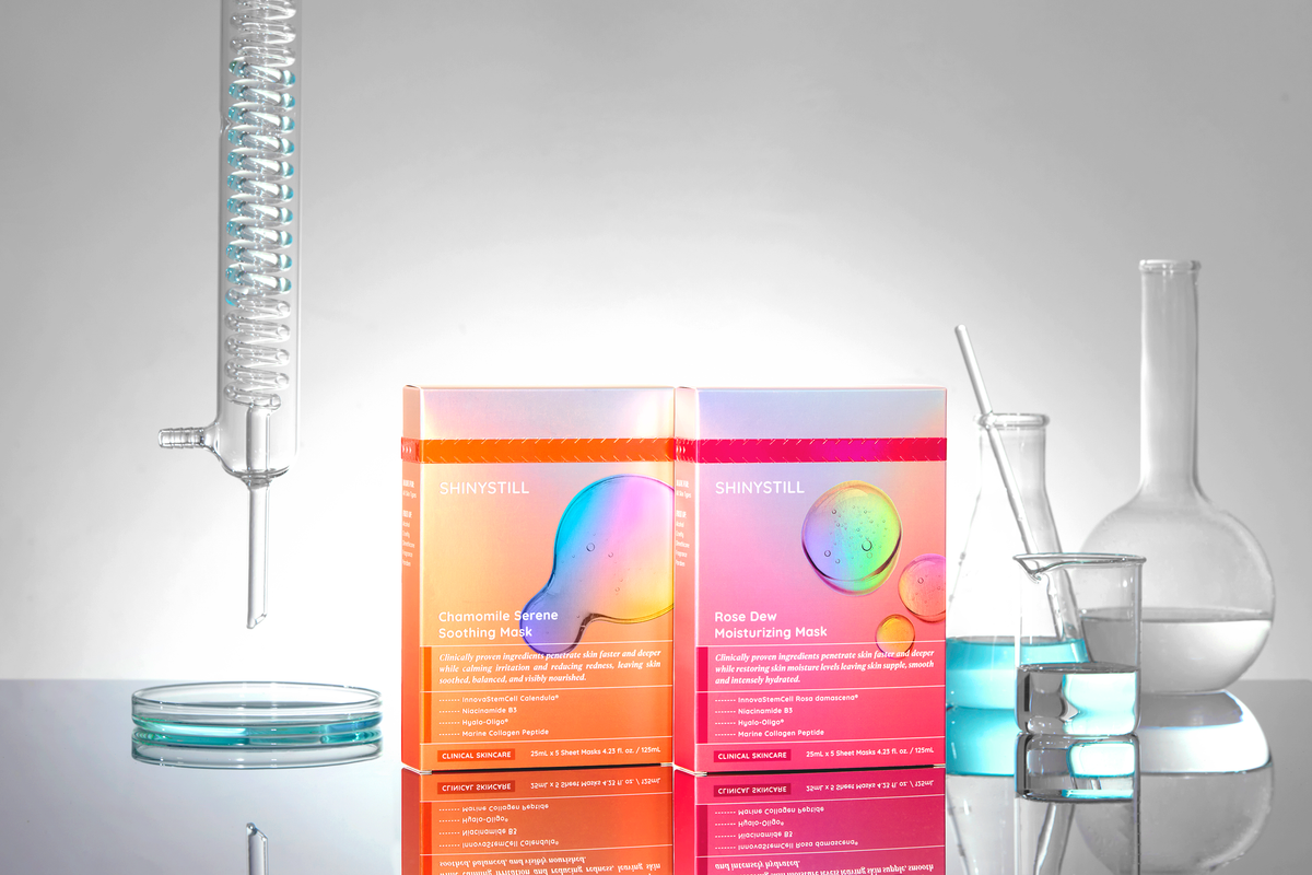 Two colorful skincare product boxes with laboratory equipment on a reflective surface.